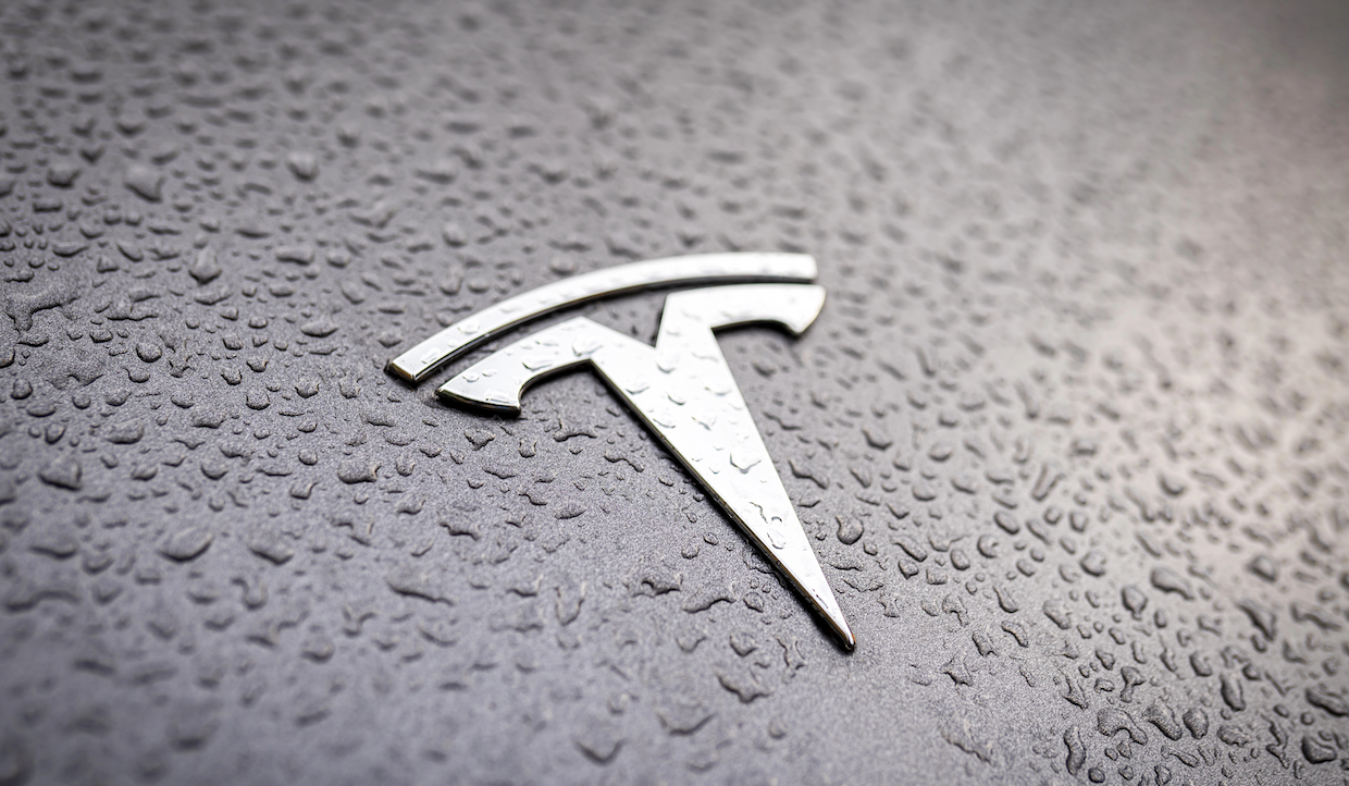 Primo piano del logo Tesla su una superficie ricoperta di gocce d'acqua.