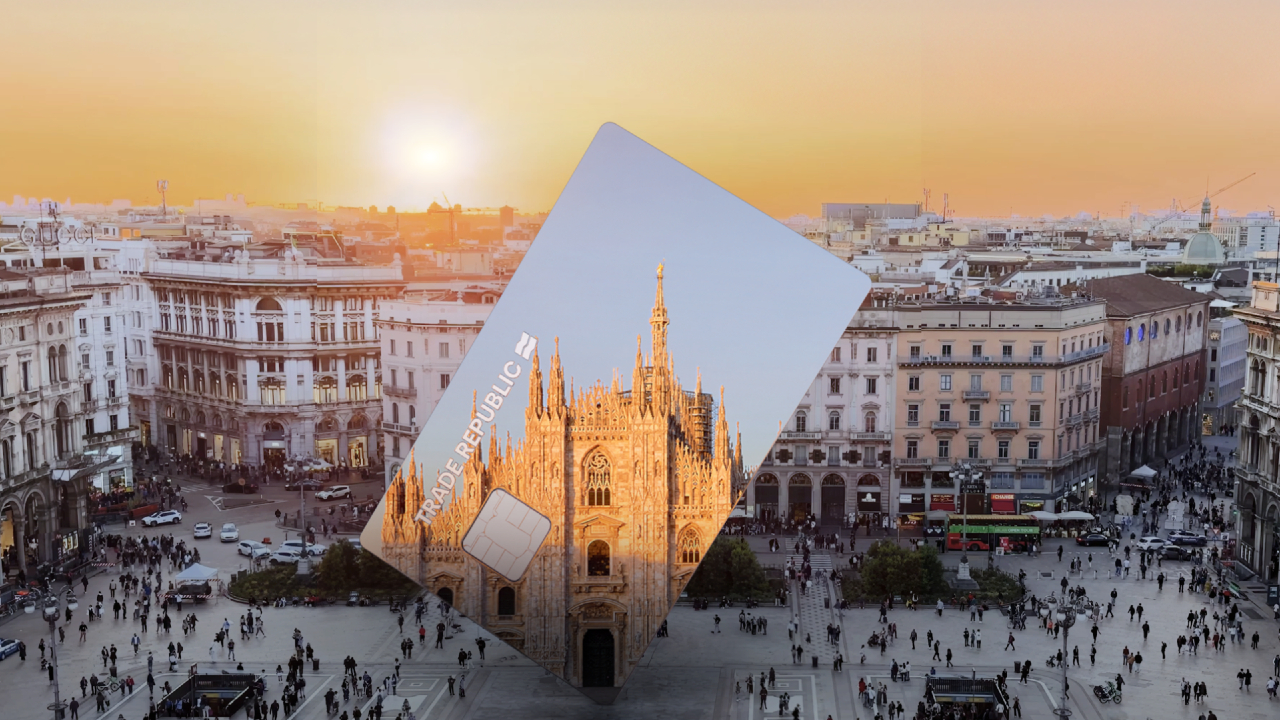 Al tramonto, il paesaggio urbano di Milano presenta il Duomo immerso in calde tonalità arancioni. Una grande carta di credito trasparente, decorata con la cattedrale e il logo della Trade Republic, è inclinata maestosamente sulla vista della città.