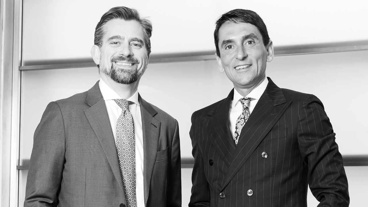 Alessandro Di Michele e Pierpaolo Fraudatario in giacca e cravatta sono in piedi uno accanto all'altro, raggianti. Di Michele, sulla sinistra, sfoggia un completo chiaro con una cravatta fantasia, mentre Fraudatario indossa un completo doppiopetto scuro a righe sottili e una cravatta decorativa. Sono in posa su uno sfondo semplice.