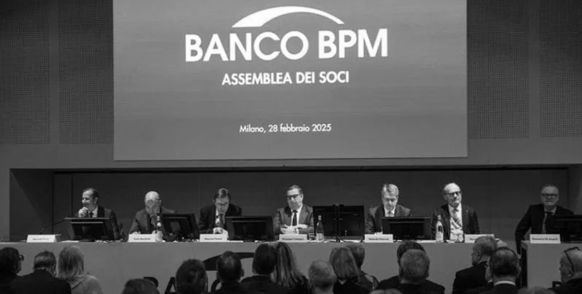 Una foto in bianco e nero che mostra un panel di conferenza con sette persone sedute a un lungo tavolo, di fronte al pubblico. Lo schermo dietro di loro mostra il logo del Banco BPM e il testo "Assemblea dei soci, Milano, 28 febbraio 2025.