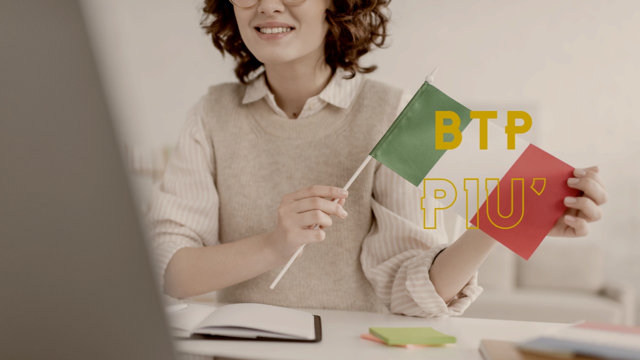 Persona che tiene in mano una bandiera italiana mentre sorride a una scrivania, con la scritta "BTP PIÙ" in verde e giallo accanto. Un quaderno e dei post-it colorati sono sul tavolo.