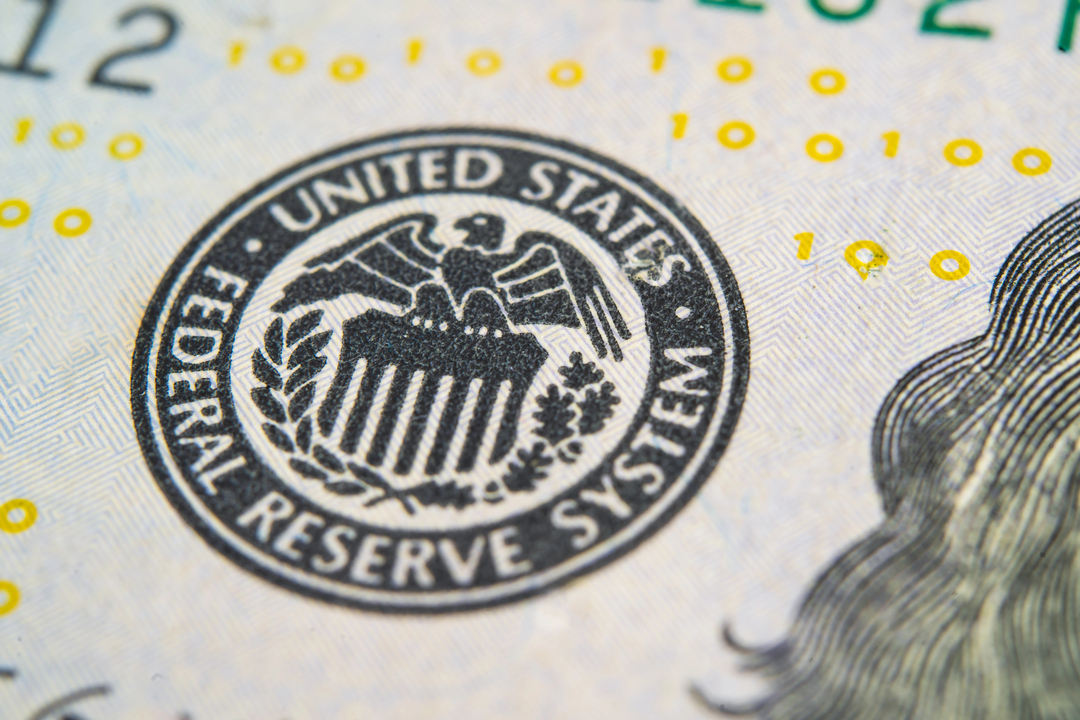 Primo piano del sigillo del Federal Reserve System degli Stati Uniti su una banconota. L'emblema in bianco e nero raffigura un'aquila con le ali spiegate che regge uno scudo, che mette in risalto l'autorità della Federal Reserve, circondata da una corona e stelle. Sono visibili i dettagli della texture della banconota.