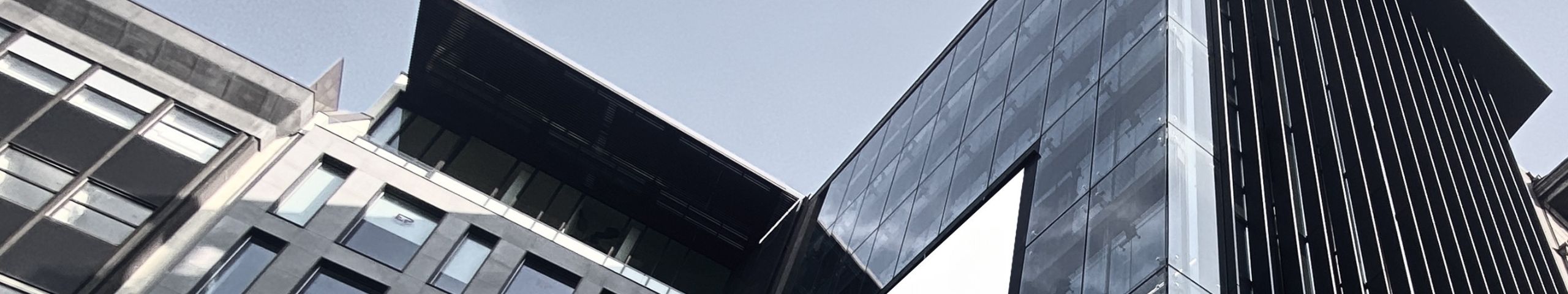 Moderni edifici per uffici con facciate in vetro e metallo, caratterizzati da angoli acuti e superfici riflettenti, sotto un cielo limpido.