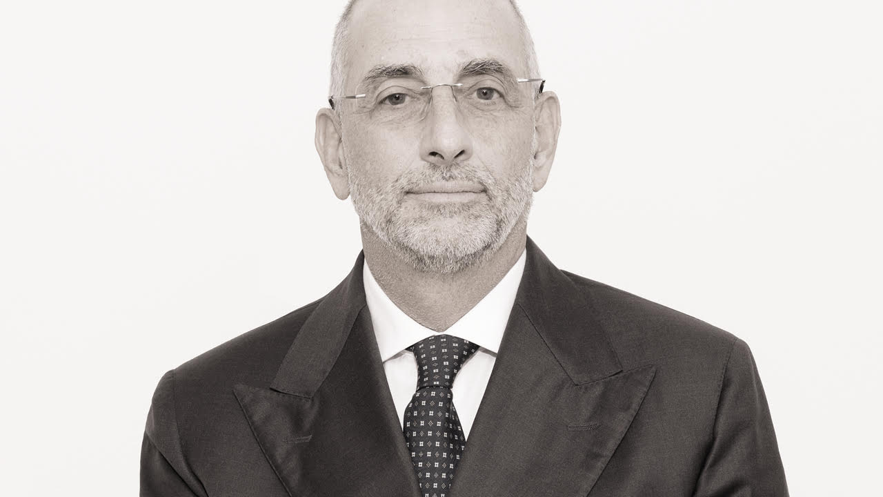 Ugo Loeser in un abito formale, impreziosito da una cravatta a pois, si staglia contro uno sfondo semplice. La sua espressione neutra completa l'eleganza senza tempo dell'immagine in bianco e nero
