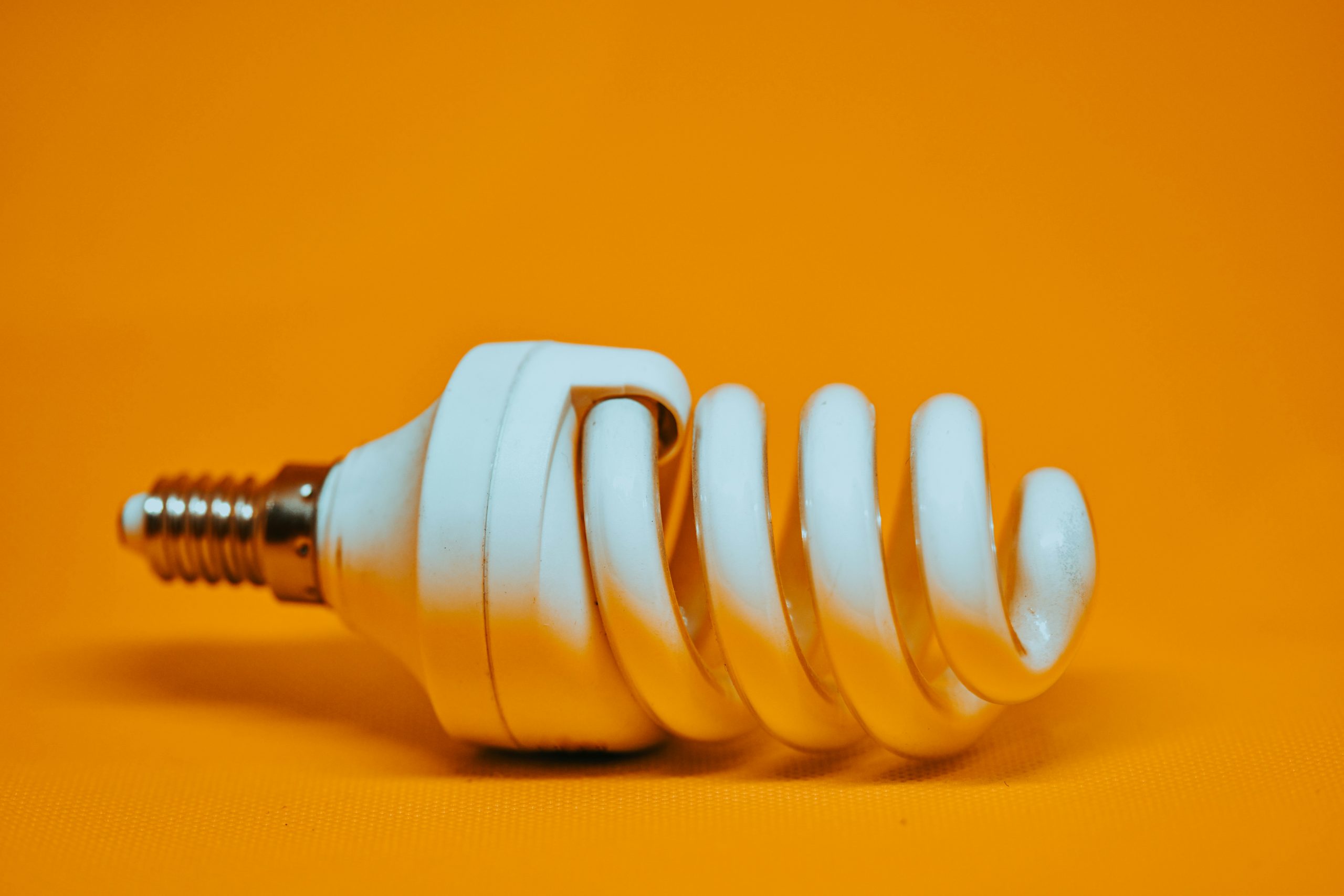 Un primo piano di una lampadina fluorescente compatta adagiata su un lato su uno sfondo arancione brillante. La lampadina, che simboleggia Vontobel transizione energetica, ha una forma a spirale e una base a vite in metallo, evidenziando il suo impegno per l'efficienza nelle soluzioni energetiche.