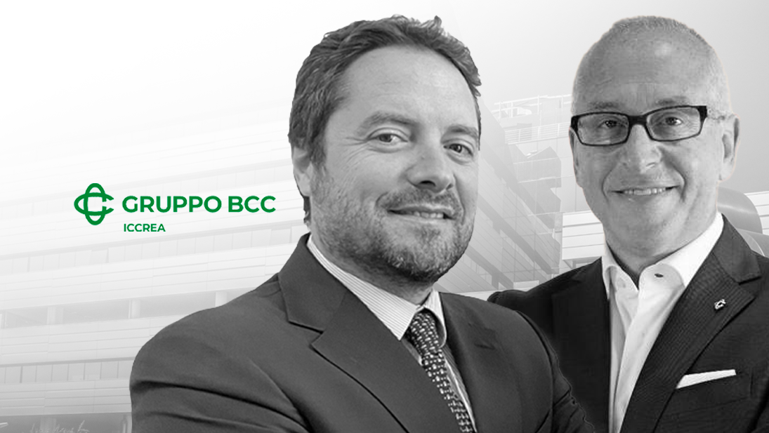 Due uomini in tailleur stanno in piedi con sicurezza davanti a un edificio decorato con il logo del Gruppo BCC Iccrea, incarnazione della competenza in formazione e consulenza. Entrambi sorridono, catturati in un'immagine senza tempo in bianco e nero sullo sfondo sfocato di una struttura architettonica.