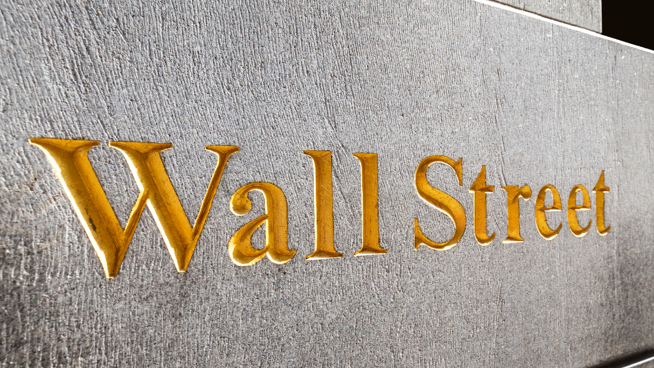 Un primo piano delle parole "Wall Street" incise in lettere dorate su una superficie di pietra. Il testo è ben visibile, a riflettere la sua associazione iconica con finanza, commercio e azioni, che simboleggia il battito cardiaco del mercato azionario.