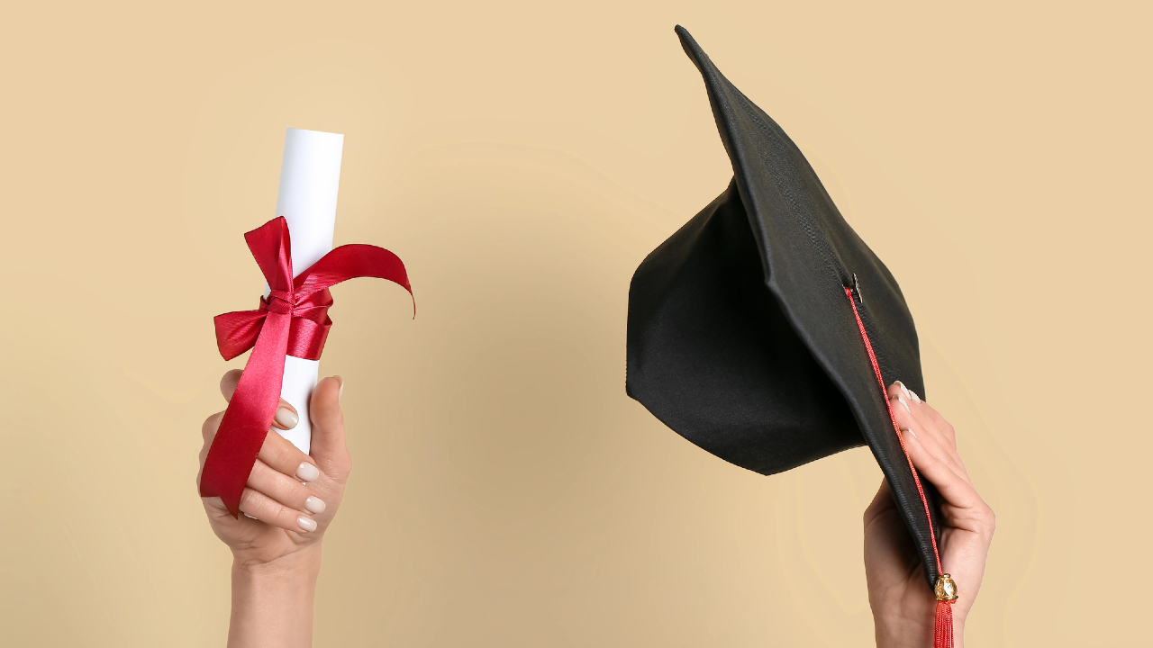 Una mano regge con orgoglio un diploma arrotolato e legato con un nastro rosso, simbolo del riscatto laurea, mentre un'altra mano tiene in equilibrio con grazia un cappello nero da laureato su uno sfondo beige tenue.