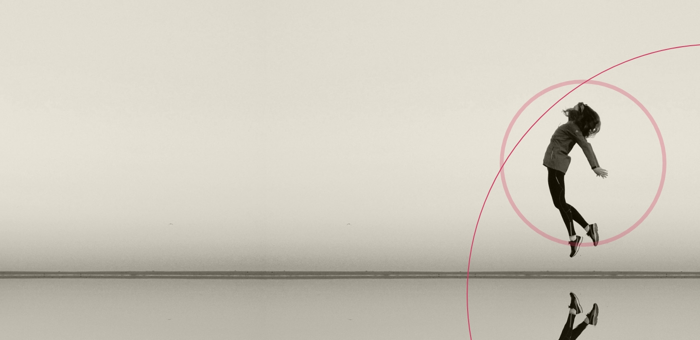Una persona che salta gioiosamente su una vasta superficie piana con uno sfondo di cielo terso. Un cerchio rosa e una linea sono sovrapposti digitalmente, aggiungendo un elemento dinamico. Il riflesso sul terreno esalta la simmetria della composizione.