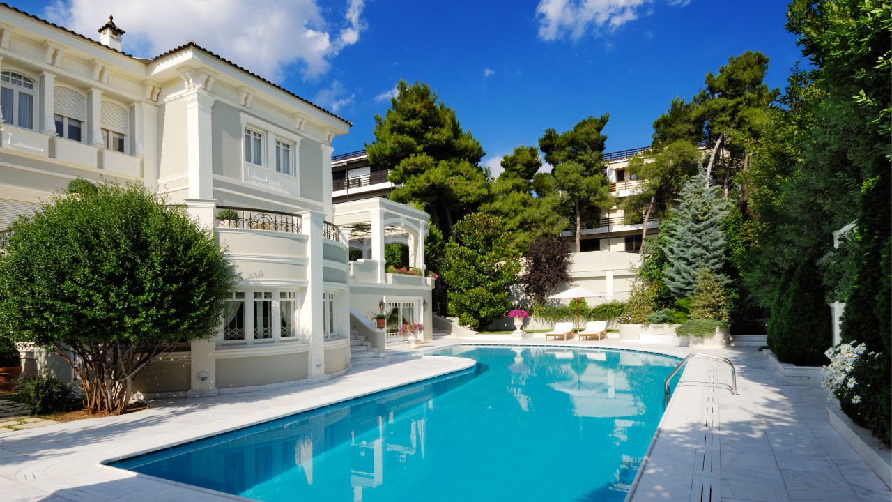 Elegante villa bianca con una grande piscina, circondata da una vegetazione lussureggiante e alberi. Esempio per indicare il settore delle case di lusso.