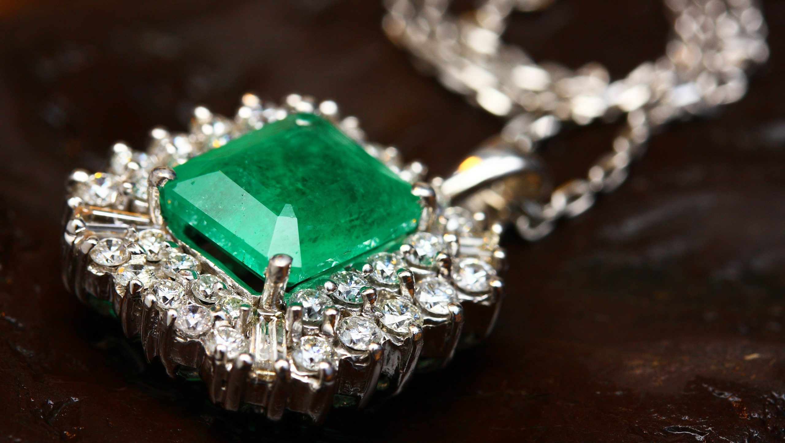 Un primo piano di un elegante pendente da collana con un grande smeraldo dal taglio quadrato circondato da scintillanti pietre preziose bianche. L'intricata montatura in argento esalta l'aspetto lussuoso della collana.