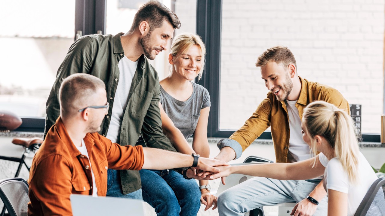 Immagine rappresentativa di una società familiare o di una impresa di famiglia, con un gruppo di cinque giovani adulti che sono riuniti in una stanza luminosa con grandi finestre.o nel lavoro di squadra.