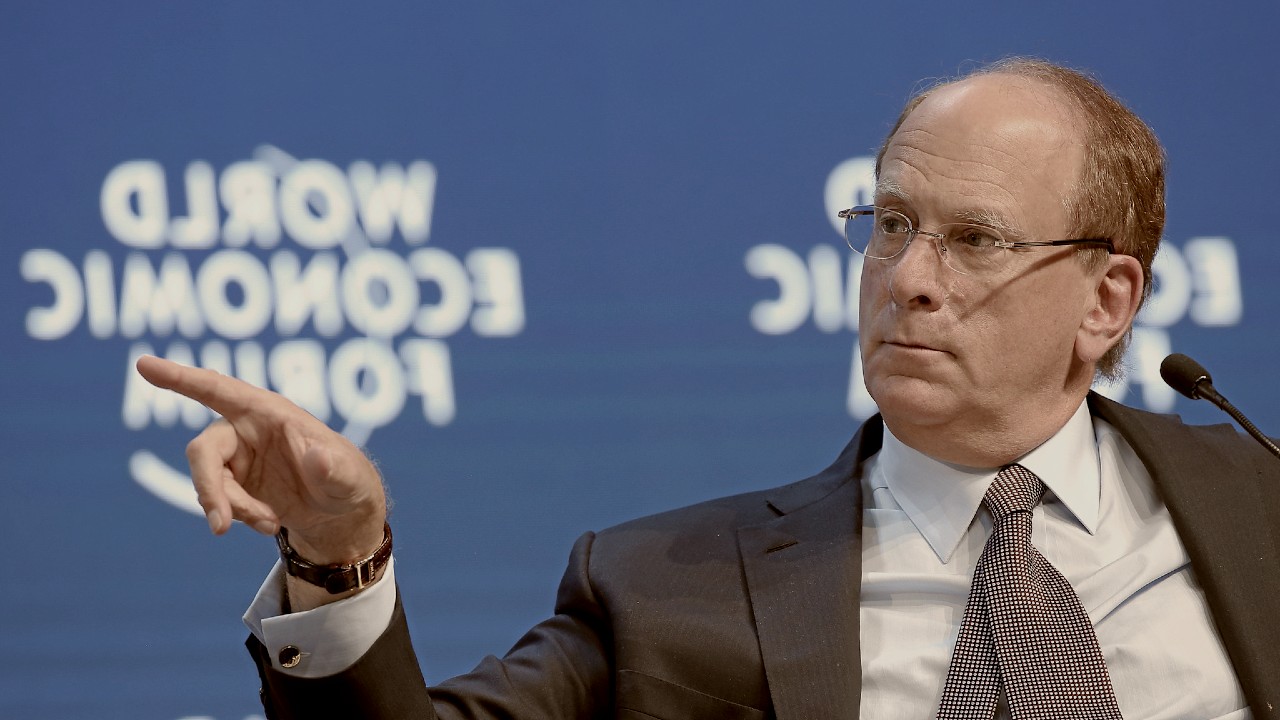Un uomo in giacca e occhiali parla a un evento, gesticolando con la mano sinistra. Sullo sfondo c'è la scritta "World Economic Forum" al contrario.