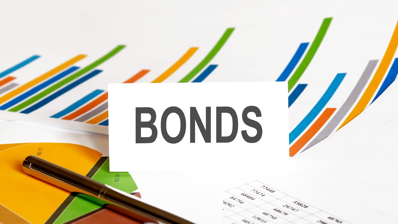 L’immagine mostra un cartoncino bianco con la parola "obbligazioni" e dei grafici colorati a barre in rialzo. Il riferimento va al tema degli investimenti: cosa fare sul mercato dei bond?