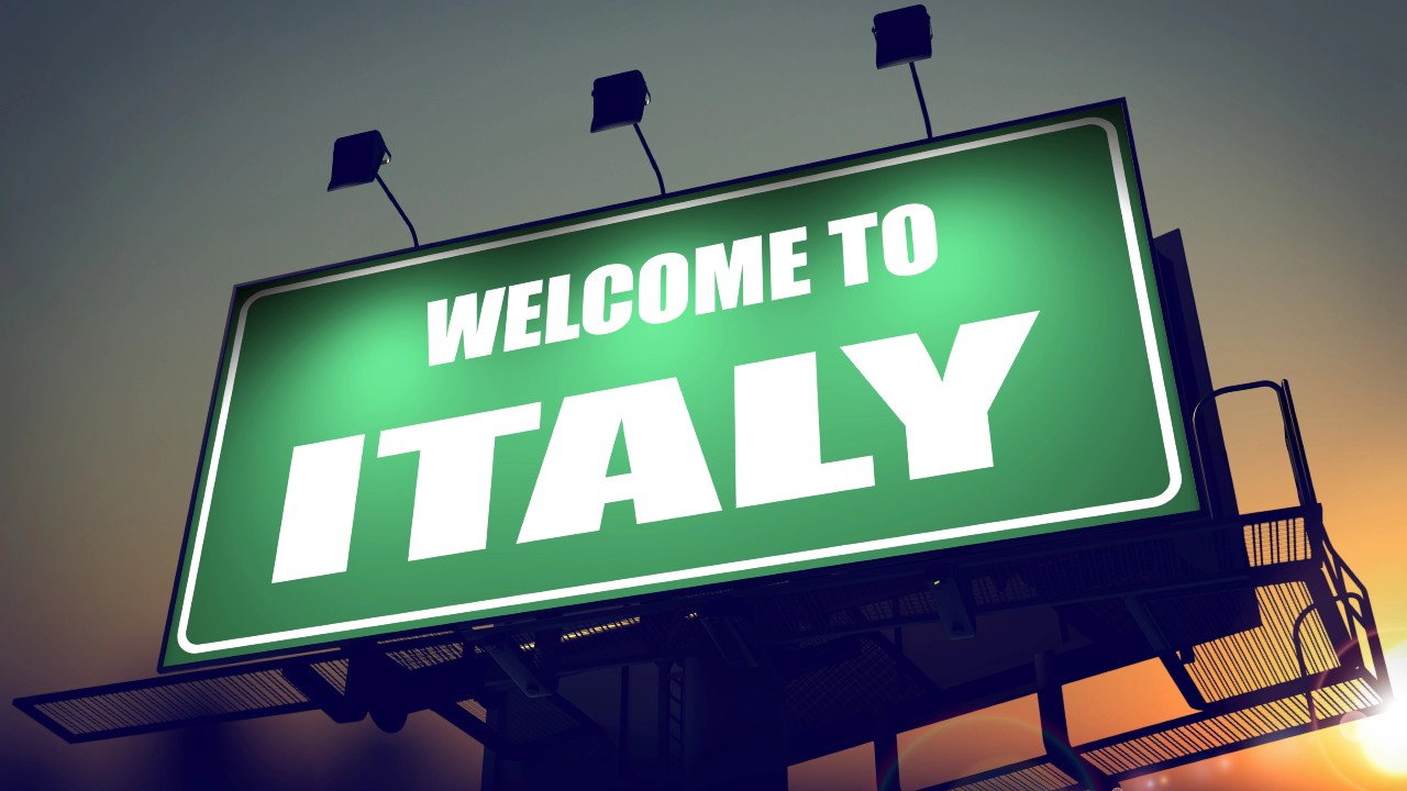 Un grande cartellone verde con la scritta bianca "Welcome to Italy" si staglia contro un cielo al tramonto, illuminato da quattro riflettori. È un caloroso benvenuto per i lavoratori che decidono di trasferirsi in Italia anche alla luce delle nuove agevolazioni fiscali previste che portano a minor tasse.