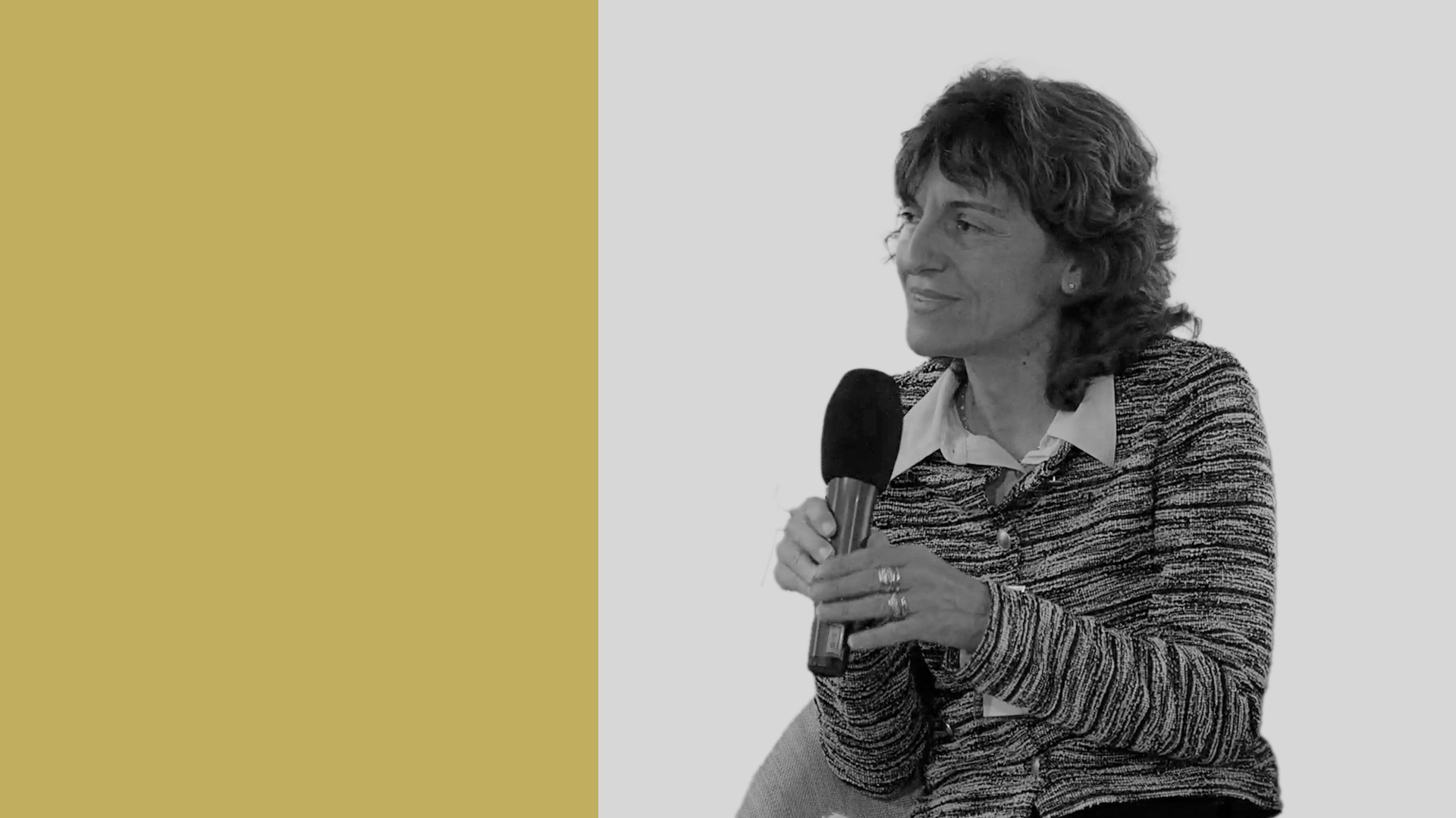 Una donna tiene in mano un microfono, sorride mentre guarda di lato. Vestita con un maglione fantasia sopra una camicia con colletto, la sua presenza trasuda calma sicurezza simile a quella di chi naviga nel mercato privato. Lo sfondo presenta giallo senape a sinistra e grigio a destra, creando un contrasto moderno.