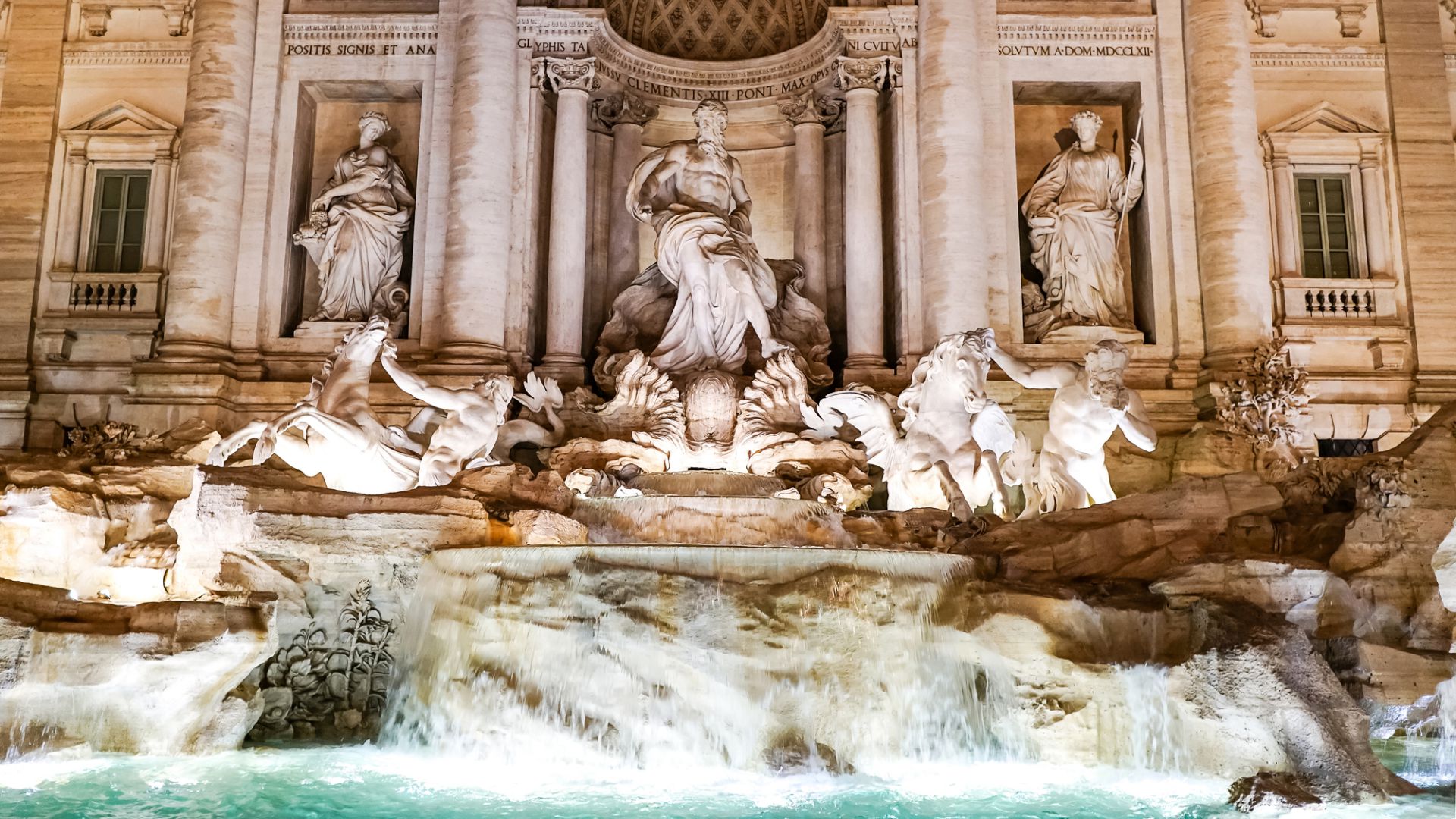 Fontana di Trevi illuminata a Roma di notte, che mette in mostra sculture intricate e acqua che scorre. Figura centrale circondata da cavalli e altre statue, con dettagli architettonici ornati sullo sfondo.