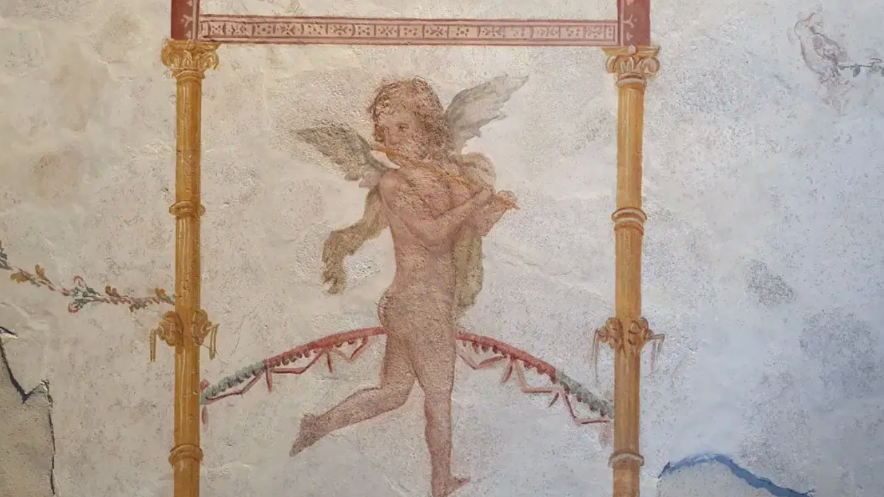 Affresco romano antico raffigurante una figura alata simile a un cherubino che porta un fagotto, circondata da bordure e colonne decorate. L'opera presenta uno stile classico, con colori tenui e motivi intricati.