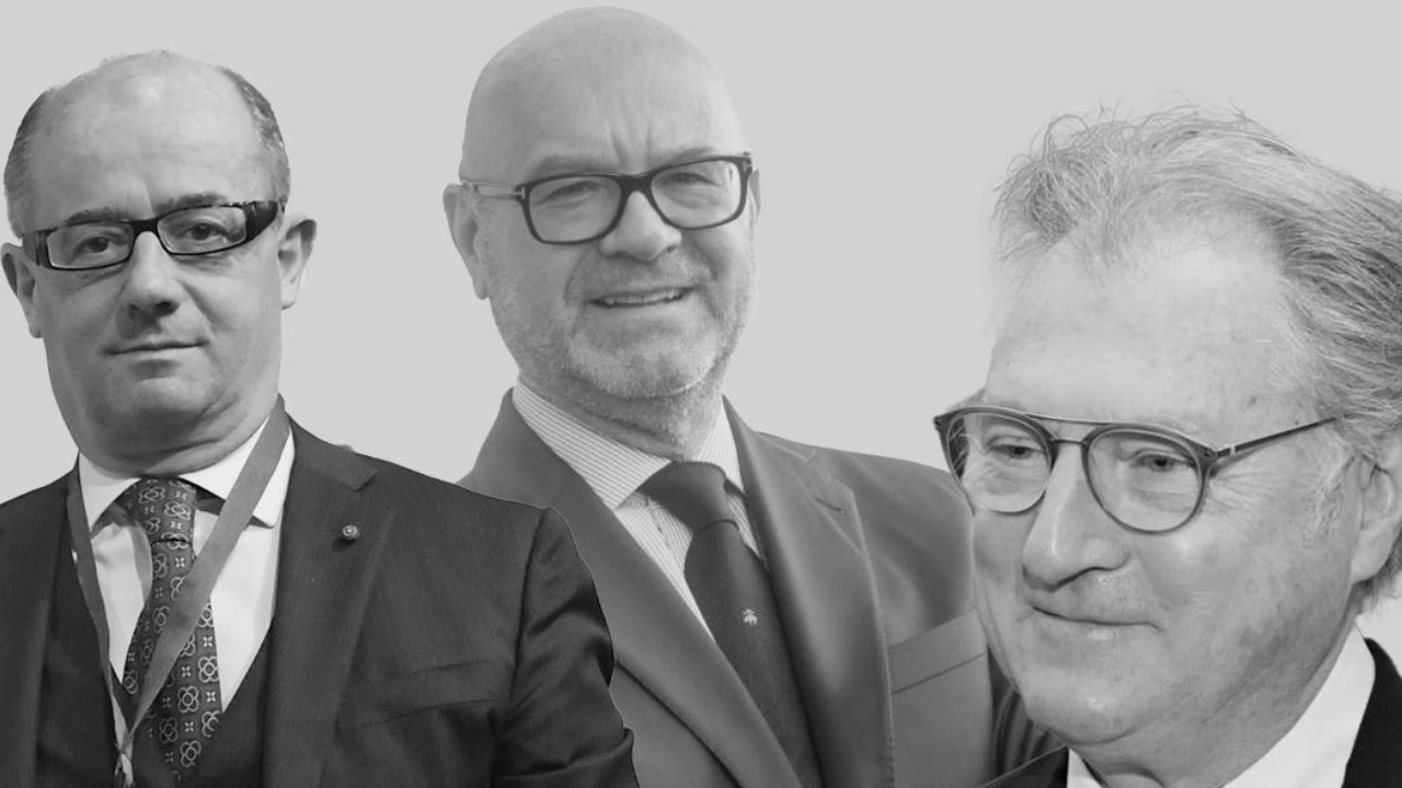Tre uomini in giacca e cravatta e occhiali sono ritratti su uno sfondo semplice. L'immagine è in bianco e nero e tutti e tre guardano in direzioni leggermente diverse, con sorrisi neutri o appena percettibili.