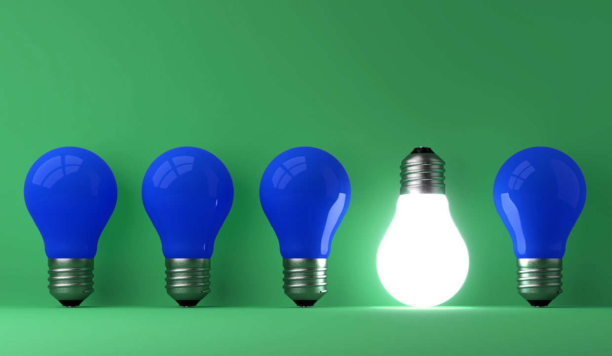 Quattro lampadine sono disposte in fila su uno sfondo verde; tre, come fondi passivi, sono blu e non illuminate, mentre la seconda da destra è bianca e brilla intensamente.