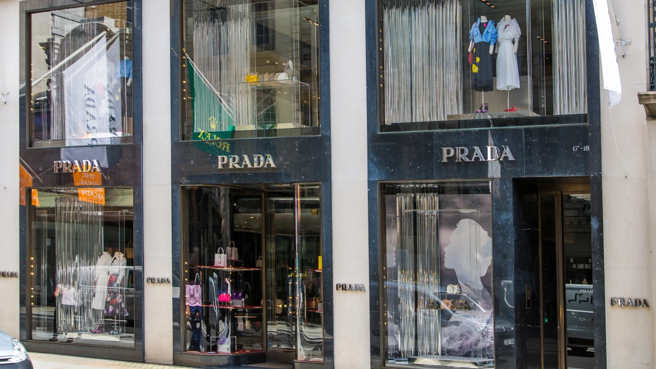 La vetrina a due piani di Prada vanta un lussuoso esterno in marmo nero e manichini in abiti eleganti. Il riferimento va a Prada che compra Versace e alla crescita dei negozi di lusso nel mondo.