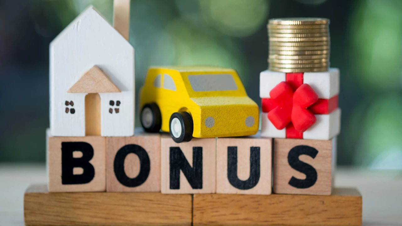 Blocchi di legno con la scritta "BONUS" sono esposti davanti a una casa giocattolo, una macchinina, una pila di monete e una scatola regalo. Il riferimento alle agevolazioni prima casa e agli altri bonus.