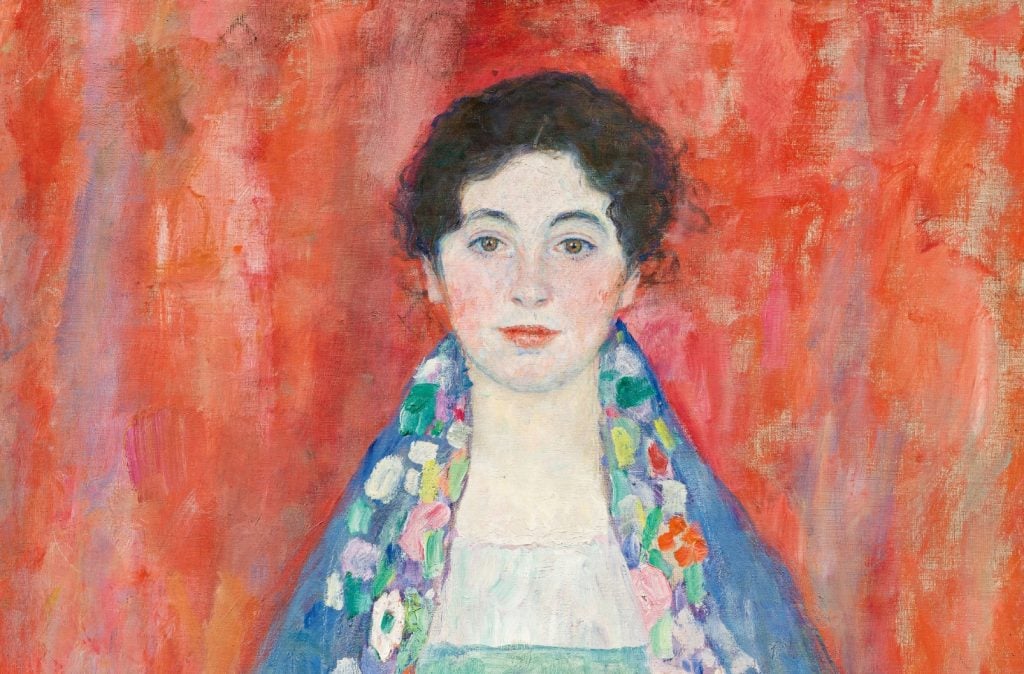 Ritratto dipinto di una donna con capelli scuri e ricci, che indossa uno scialle blu decorato con motivi floreali, su uno sfondo testurizzato di colore rosso e rosa.