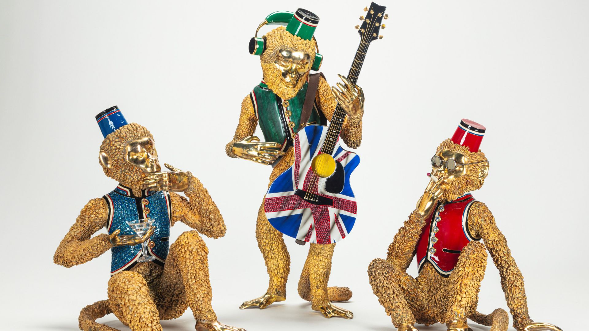 Tre statue di scimmie dorate che indossano gilet e cappelli colorati. Una suona una chitarra decorata con la bandiera del Regno Unito, un'altra ascolta con le cuffie e la terza – fedele allo stile di Stefano Gabbana Asta – è seduta a terra con una mano alla bocca.