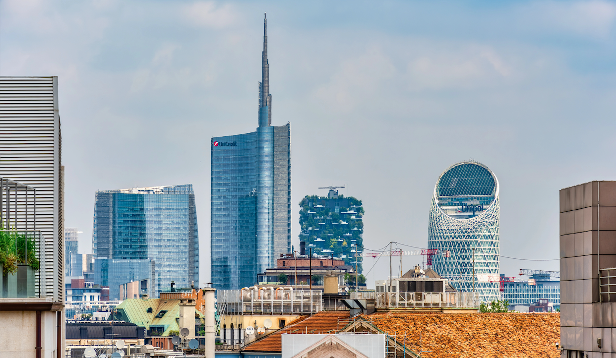 Skyline di Milano caratterizzato da moderni grattacieli, tra cui la Torre Unicredit, le torri del Bosco Verticale ricoperte di verde e il caratteristico edificio Allianz dalla forma circolare, con i tradizionali tetti in primo piano.