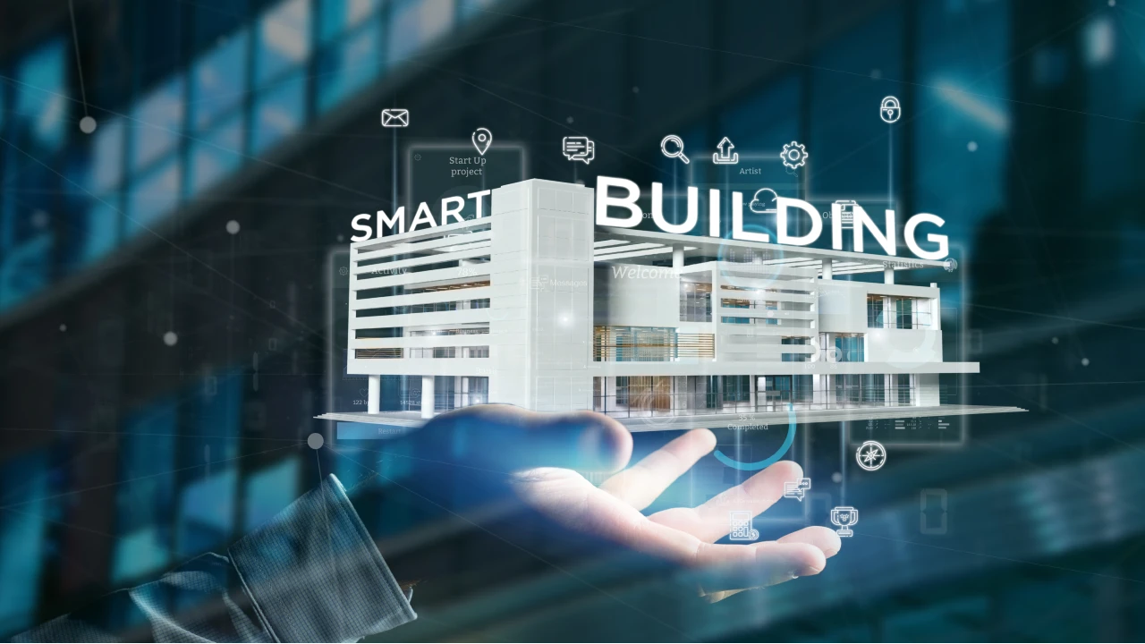 La mano di una persona tiene un modello digitale di un edificio moderno etichettato "EDIFICIO INTELLIGENTE", circondato da icone tecnologiche che rappresentano connettività, automazione e sistemi intelligenti: una visione del futuro per ogni casa nuova.