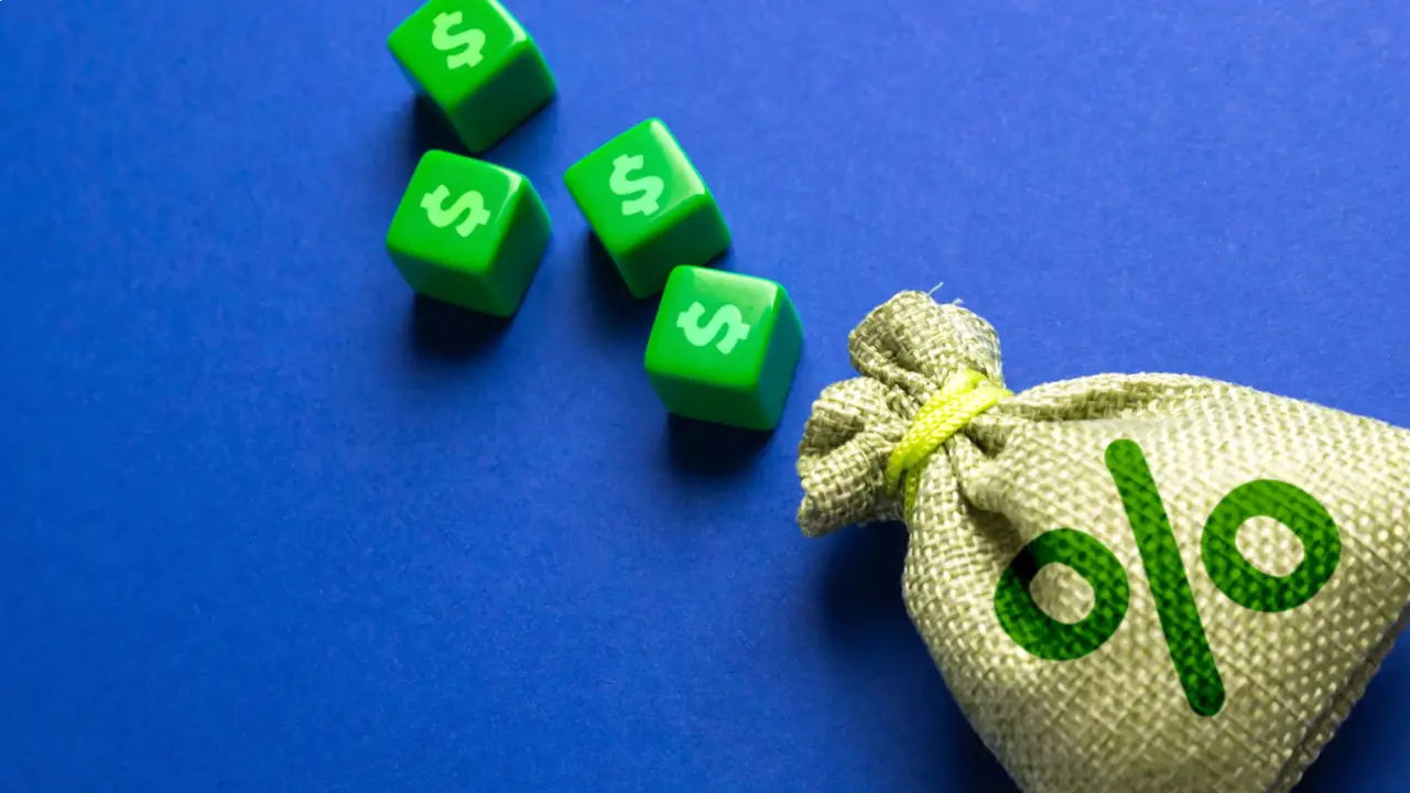 Un piccolo sacco di iuta con un simbolo percentuale verde è posizionato accanto a quattro dadi verdi con il simbolo del dollaro su sfondo blu.