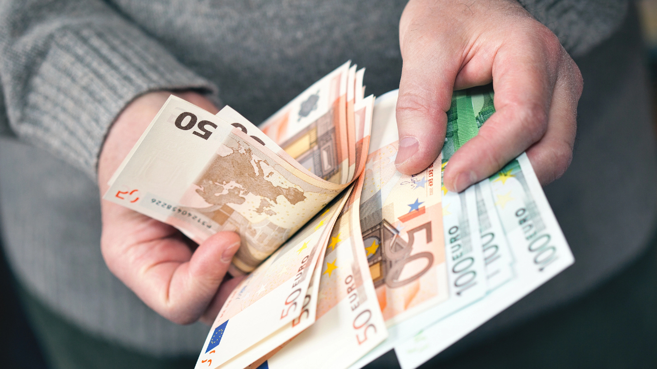 Una persona con un maglione grigio tiene in mano e conta diverse banconote in euro, tra cui quelle da 50 e 100 euro, probabilmente in cerca di una consulenza su questioni finanziarie.