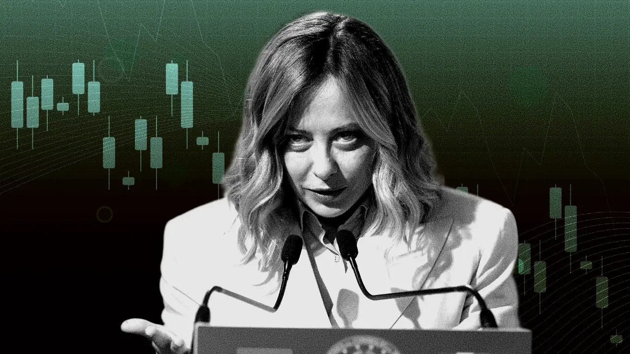 Una donna con i capelli lunghi fino alle spalle parla da un podio con due microfoni. Indossa una giacca chiara e sullo sfondo si vedono grafici astratti di borsa.
