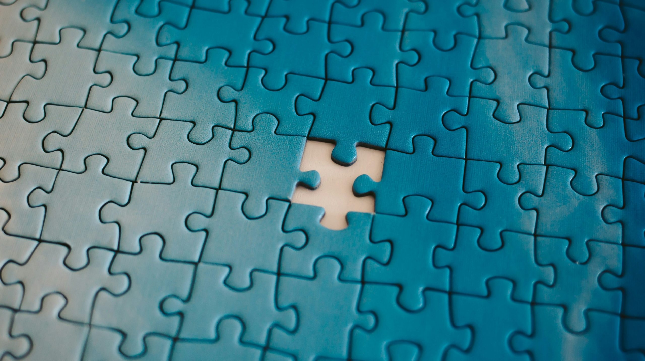 Primo piano di un puzzle blu a cui manca un pezzo, lasciando intravedere uno spazio bianco vuoto in cui dovrebbe inserirsi il pezzo.