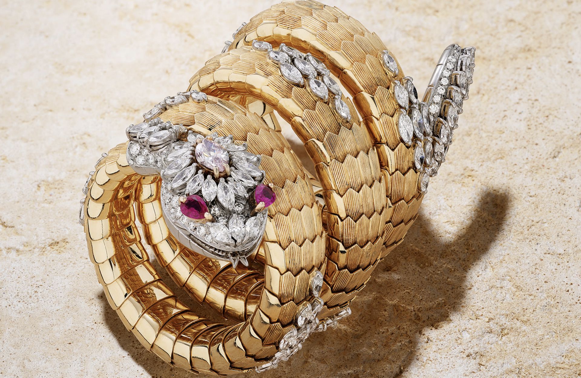 Un bracciale in oro a forma di serpente, ispirato all'orologio Bulgari Serpente, con dettagli in diamanti e pietre preziose, si snoda su una superficie leggermente strutturata, mettendo in mostra intricate squame e una squisita fattura orafa.