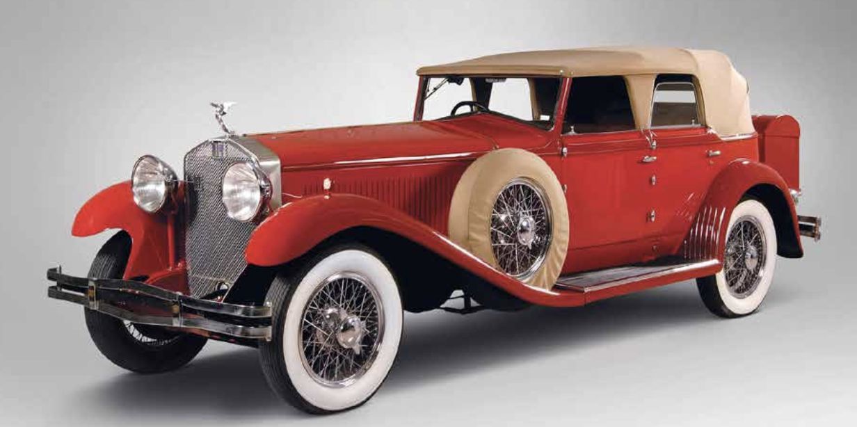 Una classica Isotta Fraschini decappottabile rossa con capote beige, dettagli cromati, grandi fari rotondi e ruota di scorta montata lateralmente, raffigurata su uno sfondo grigio semplice.