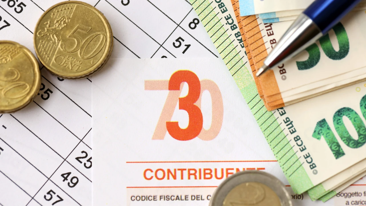Primo piano della dichiarazione dei redditi, modello 730, con monete e banconote in euro e una penna su un documento finanziario, che evidenzia detrazioni e numeri.