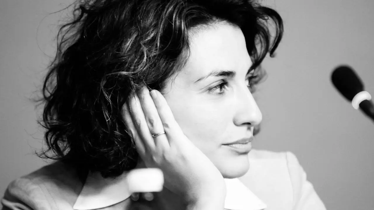 Fotografia in bianco e nero di una donna con i capelli ondulati lunghi fino alle spalle, che appoggia la testa sulla mano e guarda pensierosa di lato; in primo piano è visibile un microfono.