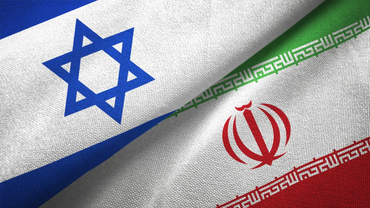 Primo piano della bandiera israeliana con la Stella di Davide blu e della bandiera iraniana con l'emblema rosso, posizionate in diagonale l'una accanto all'altra su un tessuto strutturato, a simboleggiare nazioni spesso legate da tensioni sul petrolio.