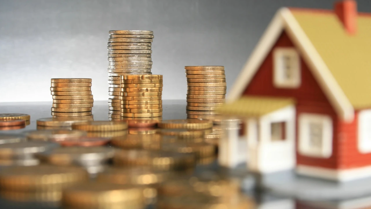 Immagine di pile di monete in primo piano con una casa sullo sfondo, per far riferimento alle opportunità d'investimento nel settore immobiliare.