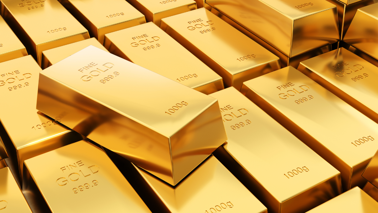 Primo piano di numerose barre d'oro luccicanti accatastate insieme, ciascuna etichettata "ORO FINO 999,9" e "1000 g", con una barra ben visibile e inclinata sopra le altre.