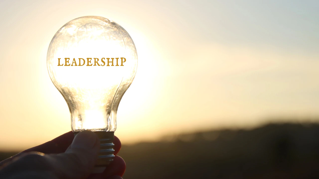 Una mano regge una lampadina con al suo interno la parola "leadeship", che brilla intensamente alla luce del sole e simboleggia la leadership innovativa.