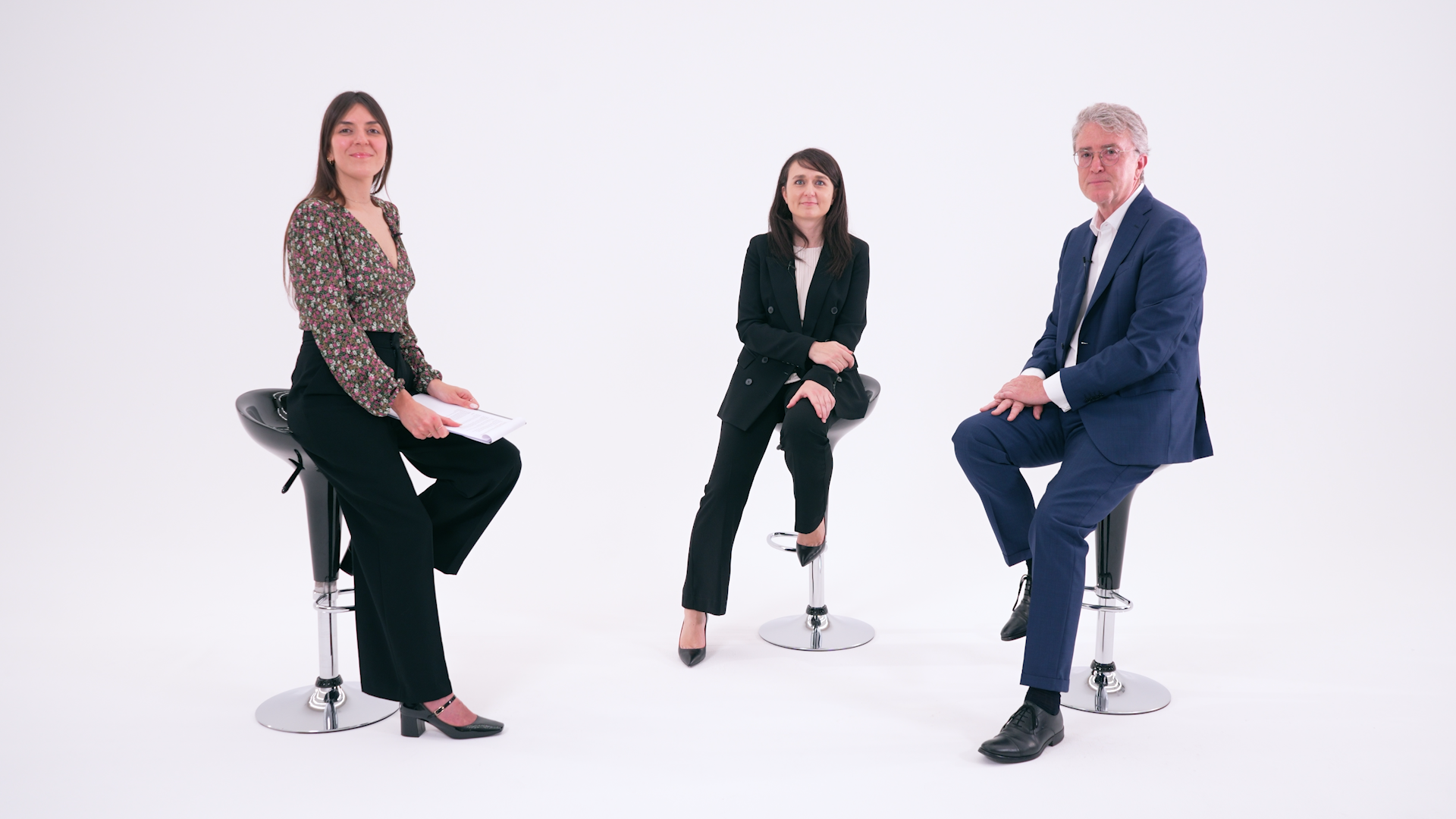Tre persone in abiti da lavoro siedono su sgabelli moderni su uno sfondo bianco. Sono ritratti due donne e un uomo in abito blu, rappresentanti professionisti del credito privato; una donna tiene in mano un blocco note e sorride alla telecamera.