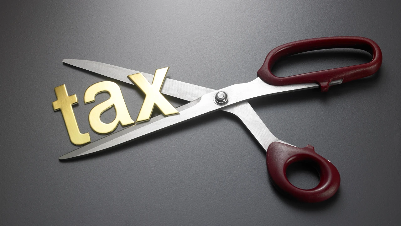 Un paio di forbici taglia la parola "tax" in lettere dorate, a simboleggiare un taglio o una riduzione delle tasse e delle ritenute. Il collegamento va alla decisione dell’Agenzia delle Entrate sulle Siiq.