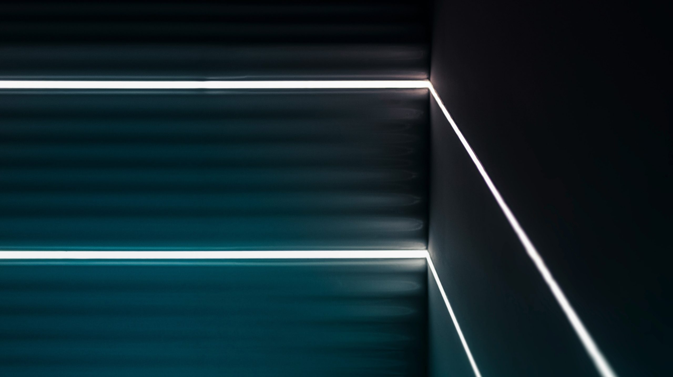 Immagine astratta di un angolo buio con strisce luminose a LED bianche orizzontali e verticali, che creano linee pulite e un aspetto minimalista e moderno con sottili sfumature blu-verdi sulle superfici delle pareti.