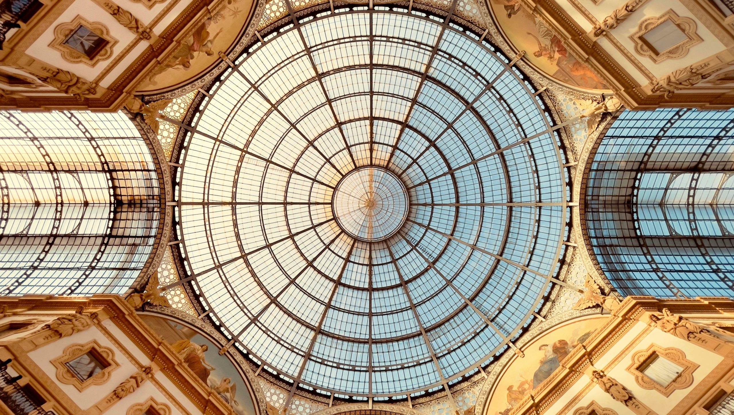 Soffitto a cupola circolare in vetro con struttura metallica a griglia, visto direttamente dal basso, circondato da elaborati dettagli architettonici: uno spazio stimolante che riflette l'eleganza spesso ricercata in contesti di itinerari previdenziali o di passaggio generazionale per famiglie.