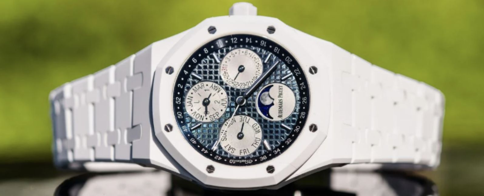 Orologio da polso di lusso orologi gioiello bianco con un dettagliato quadrante blu e argento che mostra molteplici contatori e complicazioni, su uno sfondo verde sfocato.