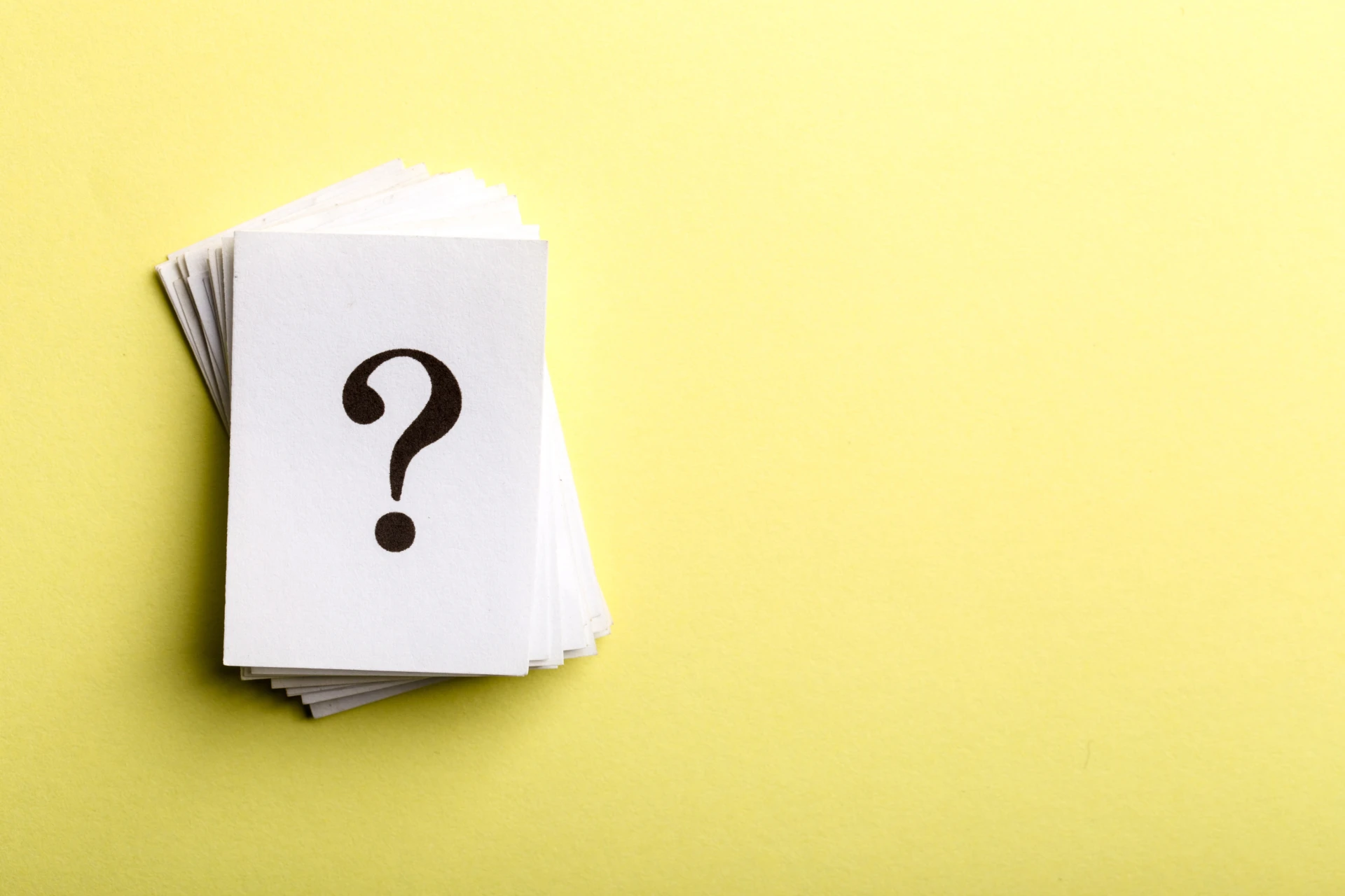 Una pila di carte bianche con un punto interrogativo nero sulla carta superiore si trova su uno sfondo giallo chiaro, catturando l'essenza di investire incertezza.