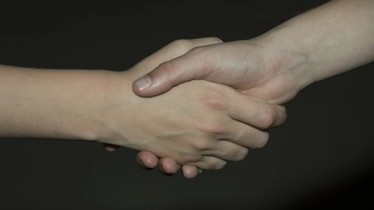 Due persone che si stringono la mano su uno sfondo scuro, simboleggiano un accordo, una collaborazione o un saluto, un'immagine che ricorda un "patto di famiglia".