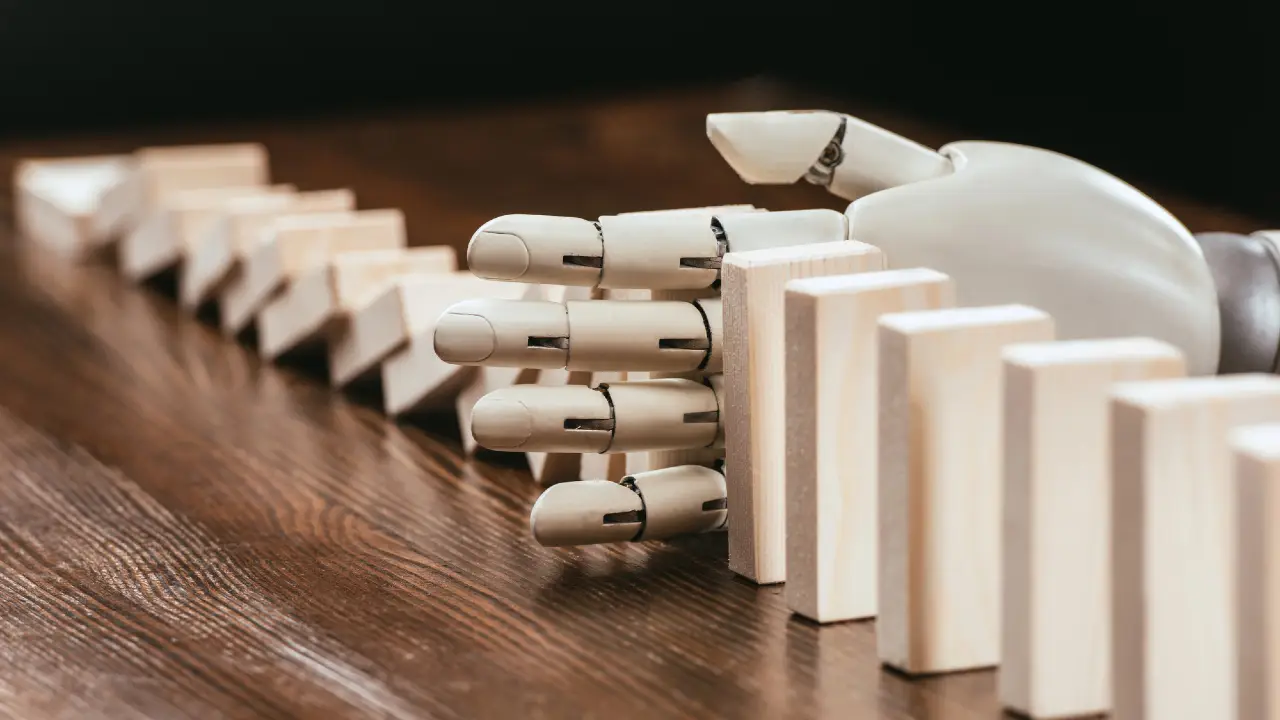 Una mano robotica ferma una fila di domino di legno in caduta su un tavolo di legno, impedendo loro di cadere ulteriormente.